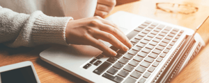 hand typing on a laptop while other hand holds coffee mug