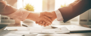 two hands shaking with business attire with desk in background